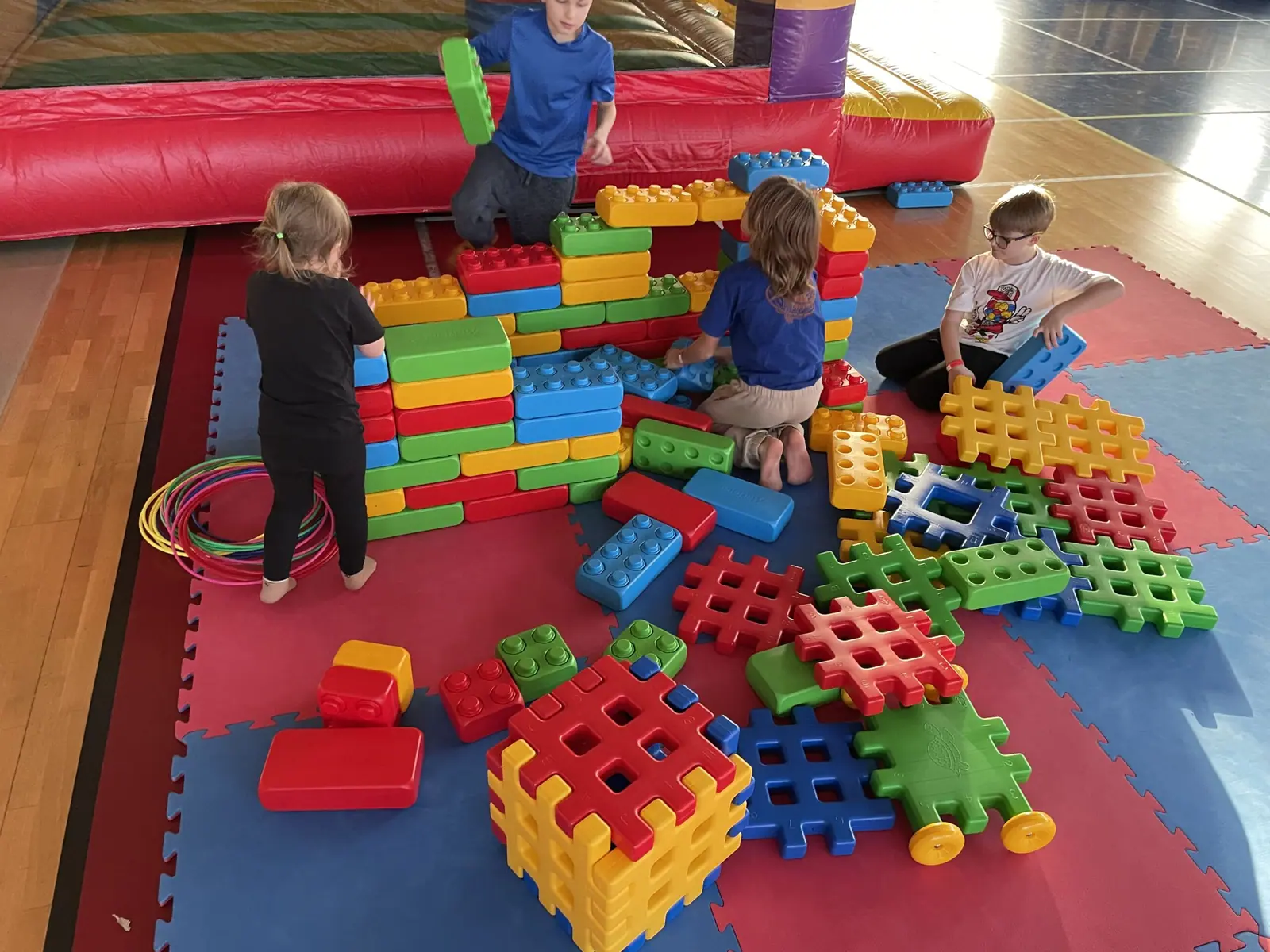 Grupa dzieci buduje z kolorowych giga klocków Lego na matach w hali