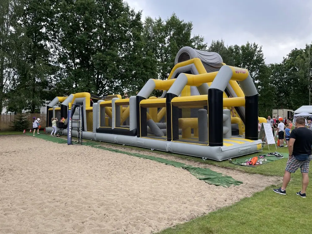 Dmuchany tor przeszkód 20 m rozstawiony na pikniku, obok uczestnicy czekają na start