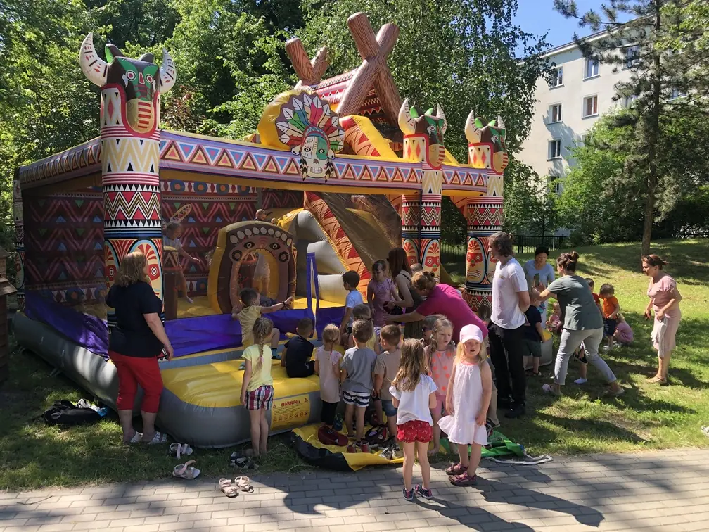 Dzieci bawią się w dmuchanym zamku Indianin ze zjeżdżalnią podczas przyjęcia na trawie