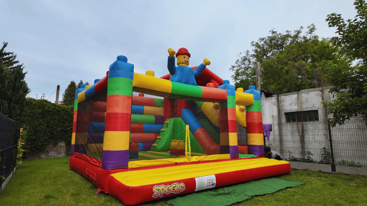 Kolorowy dmuchany Zamek Lego z figurką ludzika na dachu rozstawiony w ogrodzie